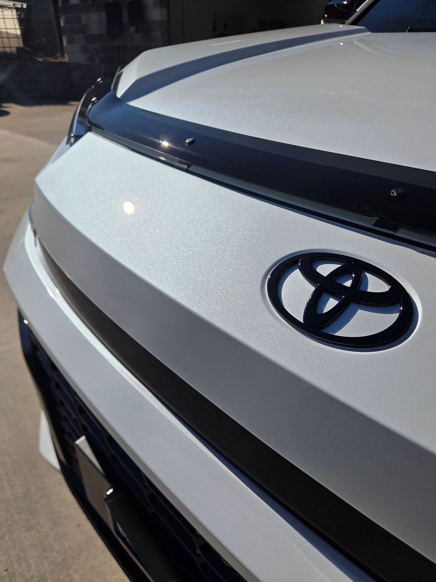 Close-up of a white Toyota RAV4's bonnet and badge, showing the paint finish